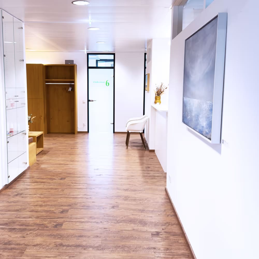 Hell beleuchteter Flur mit Holzfußboden, weißem Stuhl, offenem Holzschrank und einem Bild an der Wand.